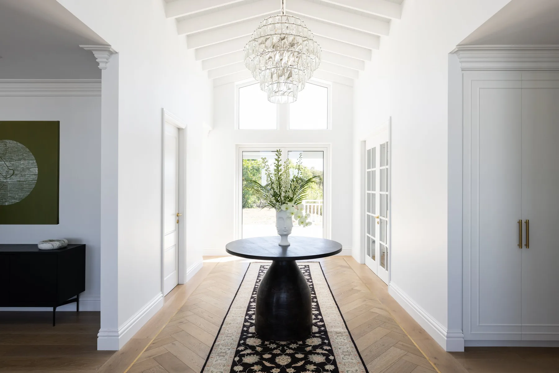 Elanora, Northern Beaches &mdash; entry hall with round black pedestal table, chandelier and herringbone timber floor