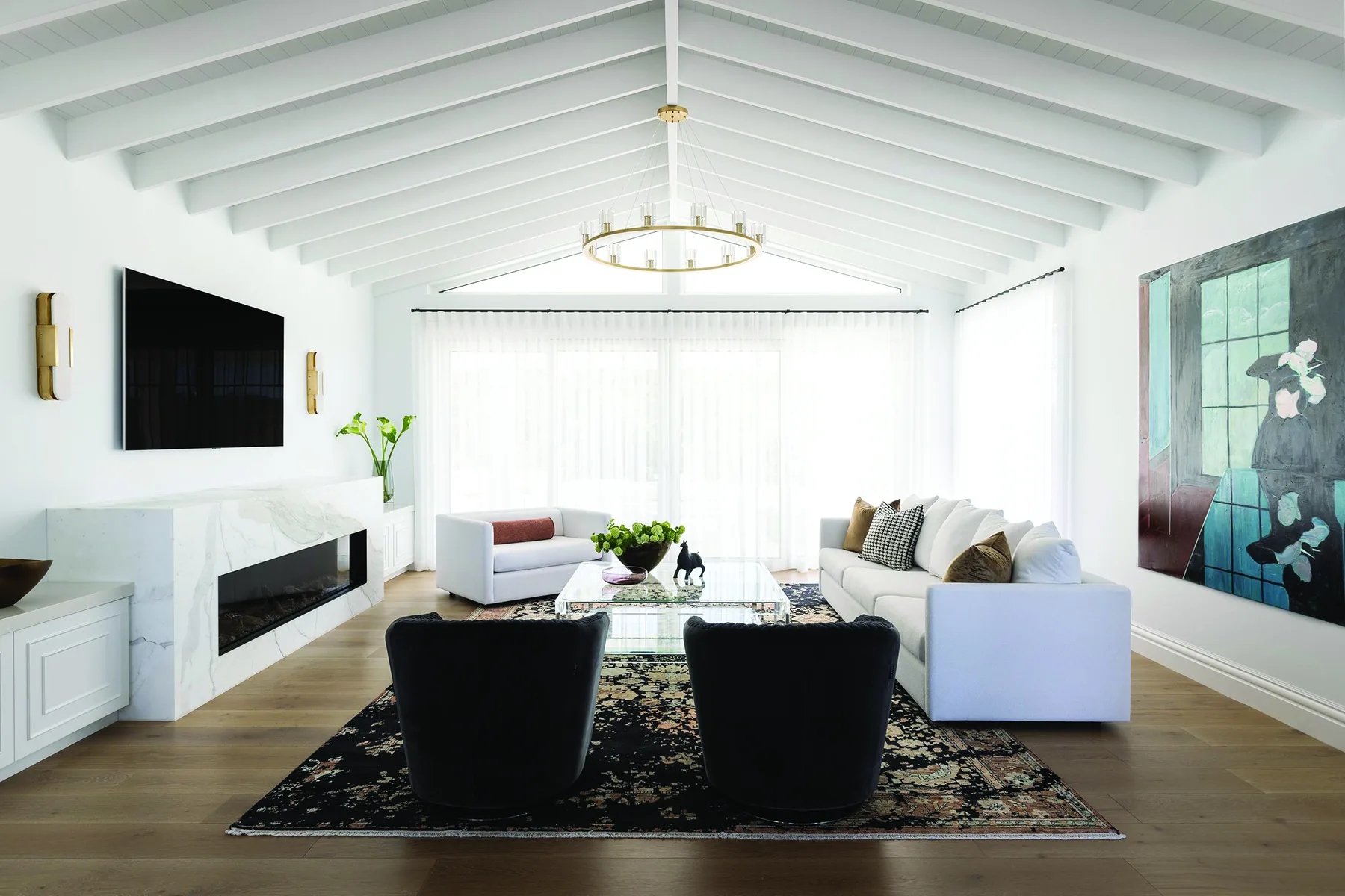 Elanora — open living room with vaulted white ceiling beams, black armchairs and marble fireplace