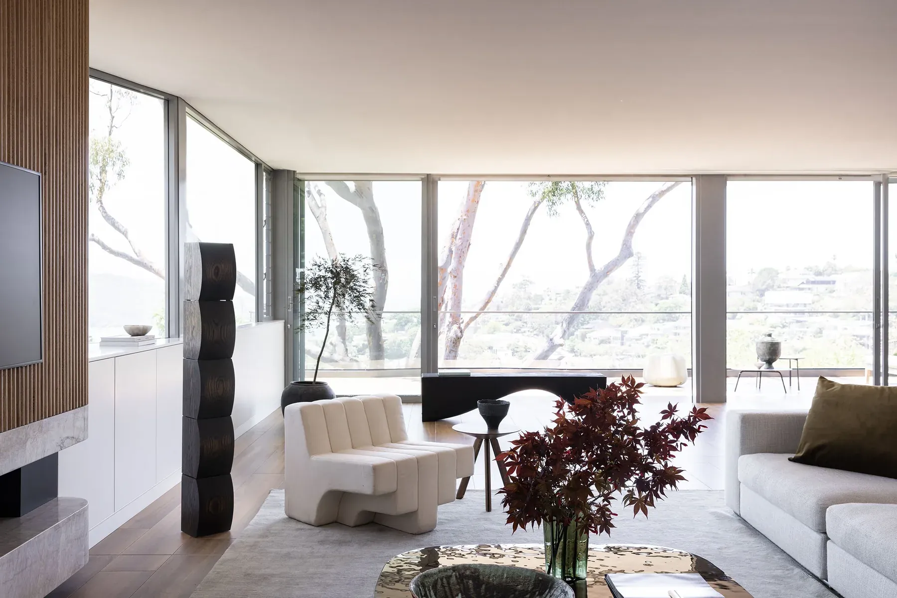 Mosman 02 &mdash; living area with treetop views, cream sculptural chair and dark red foliage